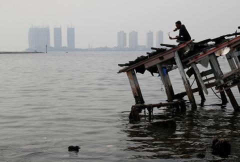 A youth stands on the wreckage of a wooden boat, during fishing with a slingshot, as smog covers North Jakarta, Indonesia, July 26, 2018. PHOTO BY REUTERS/Beawiharta