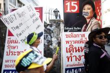 An anti-government protester hits a pre-election poster of Prime Minister Yingluck Shinawatra with a field hockey stick as his group marches through Bangkok