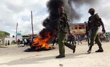 Kenyan police officers walk past a bonfire used to barricade a main road after unidentified gunmen recently attacked the coastal Kenyan town of Mpeketoni