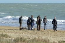 People stand next to the dead body of a migrant on the beach of Siculiana, in Western Sicily, Italy, February 19, 2016. PHOTO BY REUTERS/Guglielmo Mangiapane