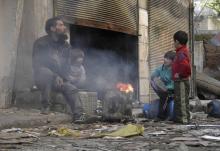 A man and children sit around a fire in the besieged area of Homs