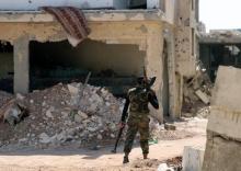 A Free Syrian Army fighter carries weapons as he walks past damaged buildings in a rebel-held part of the southern city of Deraa, Syria, July 9, 2017. PHOTO BY REUTERS/Alaa Al-Faqir