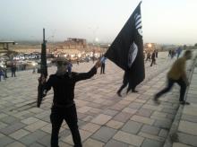 A fighter of the Islamic State of Iraq and the Levant (ISIL) holds an ISIL flag and a weapon on a street in the city of Mosul