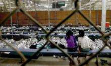 Two young girls watch a soccer match on a television from their holding area where hundreds of mostly Central American immigrant children are being processed and held at the U.S. Customs and Border Protection Nogales Placement Center in Nogales, Arizona, June 18, 2014. PHOTO BY REUTERS/Ross D. Franklin