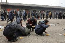 Migrants eat as others stand in line to receive free food outside a derelict customs warehouse in Belgrade, Serbia, December 22, 2016. PHOTO BY REUTERS/Marko Djurica