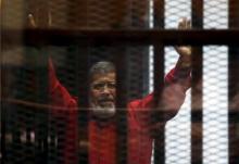 Deposed President Mohamed Mursi greets his lawyers and people from behind bars at a court wearing the red uniform of a prisoner sentenced to death, during his court appearance with Muslim Brotherhood members on the outskirts of Cairo, Egypt, June 21, 2015. PHOTO BY REUTERS/Amr Abdallah Dalsh