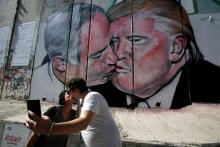 Tourists kiss each other as they stand in front of a mural depicting U.S. President Donald Trump and Israel's Prime Minister Benjamin Netanyahu kissing each other in the West Bank city of Bethlehem, October 29, 2017. PHOTO BY REUTERS/Mussa Qawasma