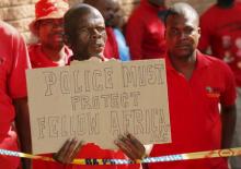 Demonstrator holds a placard outside a court in Johannesburg's Alexandra township as four men appeared in court for the killing of a Mozambican man, April 21, 2015. PHOTO BY REUTERS/Mike Hutchings