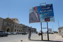 A man stands next to an election campaign poster for Wanes Al Sharef, a candidate vying for a seat in Libya's House of Representatives, in Benghazi