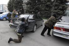 Pro-Russian armed men take cover behind cars near the local police headquarters in Luhansk, eastern Ukraine