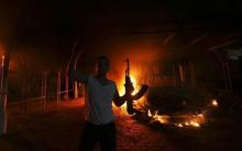A protester reacts as the U.S. Consulate in Benghazi is seen in flames during a protest by an armed group said to have been protesting a film being produced in the United States, September 11, 2012. PHOTO BY REUTERS/Esam Al-Fetori