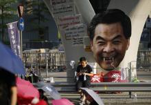 A protester sits next to a defaced cut-out of Hong Kong Chief Executive Leung Chun-ying while blocking a street outside the government headquarters in Hong Kong