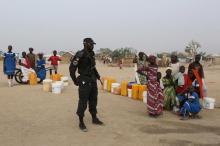 A Cameroonian police officer stands next to people waiting to fill jerrycans with water at the Minawao refugee camp for Nigerians who have fled Boko Haram attacks in Minawao, Cameroon, March 15, 2016. photo by REUTERS/Joe Penney