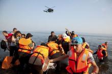 Frontex helicopter patrols over Syrian refugees arriving on an overcrowded dinghy at a beach at the Greek island of Lesbos, August 10, 2015. PHOTO BY REUTERS/Antonis Pasvantis