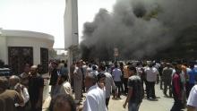 People look at smoke after a car exploded outside the parliament building, where members were drafting the new Libyan constitution, in Al Bayda