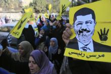 Supporters of the Muslim Brotherhood and ousted Egyptian President Mohamed Mursi shout slogans against the military and interior ministry while holding his poster and gesturing with four fingers in front of Al Rayyan mosque