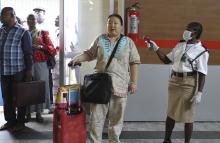 A female immigration officer uses an infra-red laser thermometer to examine a passenger