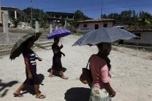 Women, whose relatives work in the U.S., use umbrellas to shield from the sun as they walk in the small villa ge of El Guantillo, outskirts of Tegucigalpa
