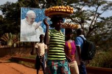 Women carrying fruits and vegetables on their heads walk past a billboard with a photograph of Pope Francis, in Bangui, Central African Republic, November 26, 2015. PHOTO BY REUTERS/Siegfried Modola