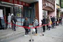 A worker in protective suit stands at the entrance of a pharmacy while people queue to enter, as the country is hit by an outbreak of the new coronavirus, in Beijing, China, February 24, 2020. PHOTO BY REUTERS/Carlos Garcia Rawlins