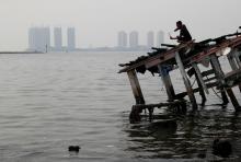A youth stands on the wreckage of a wooden boat, during fishing with a slingshot, as smog covers North Jakarta, Indonesia, July 26, 2018. PHOTO BY REUTERS/Beawiharta
