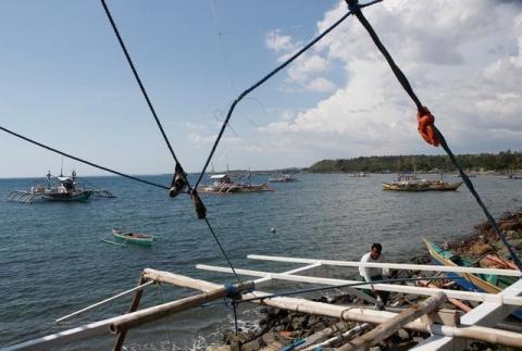 A fisherman repairs his boat overlooking fishing boats that fish in the disputed Scarborough Shoal in the South China Sea, at Masinloc, Zambales, in the Philippines, April 22, 2015. PHOTO BY REUTERS/Erik De Castro