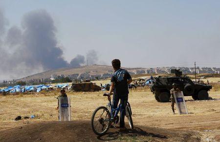 A Turkish Kurdish boy stands near the Mursitpinar border gate in Suruc in Sanliurfa province, Turkey, as smoke rises in the Syrian town of Kobani in the background, June 27, 2015. PHOTO BY REUTERS/Murad Sezer