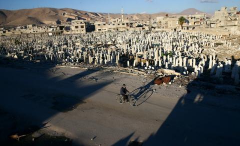 A civilian rides a bicycle past a cemetery in the rebel held besieged Douma neighbourhood of Damascus, Syria, January 3, 2017. PHOTO BY REUTERS/Bassam Khabieh