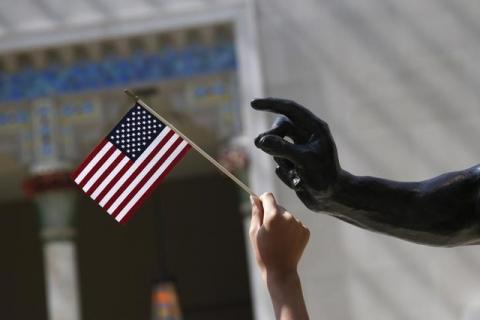 A girl holds a U.S. flag next to a sculpture after a naturalization ceremony at The Metropolitan Museum of Art in New York, July 22, 2014. PHOTO BY REUTERS/Shannon Stapleton