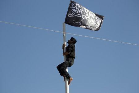 A member of al Qaeda's Nusra Front climbs a pole where a Nusra flag was raised at a central square in the northwestern city of Ariha, after a coalition of insurgent groups seized the area in Idlib province, May 29, 2015. PHOTO BY REUTERS/Khalil Ashawi