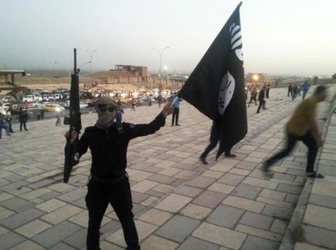 A fighter of the Islamic State of Iraq and the Levant (ISIL) holds an ISIL flag and a weapon on a street in the city of Mosul, June 23, 2014. PHOTO BY REUTERS/Stringer