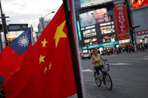A woman rides a bike past Taiwan and China national flags during a rally held in Taipei, Taiwan, May 14, 2016. PHOTO BY REUTERS/Tyrone Siu