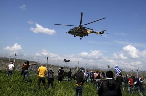 Migrants and refugees react as a Macedonian police helicopter flies over during clashes next to a border fence at a makeshift camp at the Greek-Macedonian border near the village of Idomeni, Greece, April 10, 2016. PHOTO BY REUTERS/Stoyan Nenov