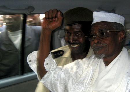 Former Chad President Hissene Habre (R) raises his fist in the air as he leaves a court in Dakar escorted by a Senegalese policeman in this November 25, 2005 file photo. PHOTO BY REUTERS/Aliou Mbaye