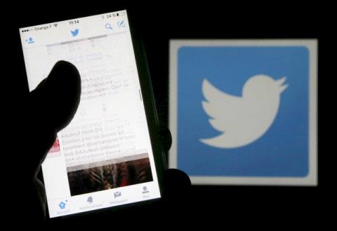 A man reads tweets on his phone in front of a displayed Twitter logo in Bordeaux, southwestern France, March 10, 2016. PHOTO BY REUTERS/Regis Duvignau/Illustration