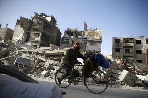 A handicapped man rides a bicycle past damaged buildings in the besieged town of Douma in eastern Ghouta in Damascus, Syria, March 1, 2018. PHOTO BY REUTERS/Bassam Khabieh
