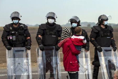 A migrant carries a child as she waits for a bus in front of riot police after crossing into Hungary from the border with Serbia on a field near the village of Roszke, September 5, 2015. PHOTO BY REUTERS/Marko Djurica