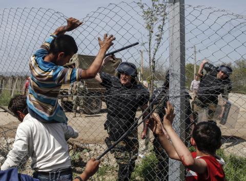 A Macedonian policeman uses his baton to prevent migrants and refugees to open the border fence at a makeshift camp at the Greek-Macedonian border near the village of Idomeni, Greece, April 7, 2016. PHOTO BY REUTERS/Marko Djurica