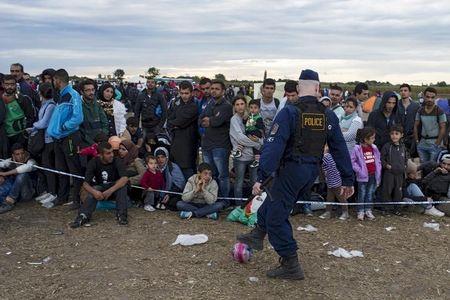 Hungarian police officer kicks a ball as migrants arrive to a collection point in the village of Roszke in Hungary after crossing the border from Serbia, September 6, 2015. PHOTO BY REUTERS/Marko Djurica