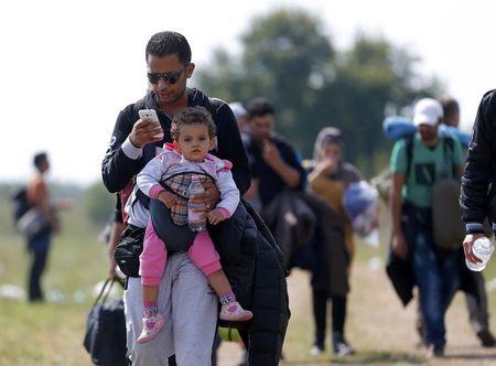 A migrant uses his mobile phone carrying his child as he walks through fields with others next to a collection point near the Serbian Hungarian border in Roszke, Hungary, September 13, 2015. PHOTO BY REUTERS/Laszlo Balogh