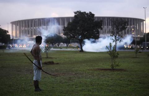 A native Brazilian stands in front of the Mane Garrincha soccer stadium as police use tear gas to impede a group of Indians from approaching it during a demonstration in Brasilia