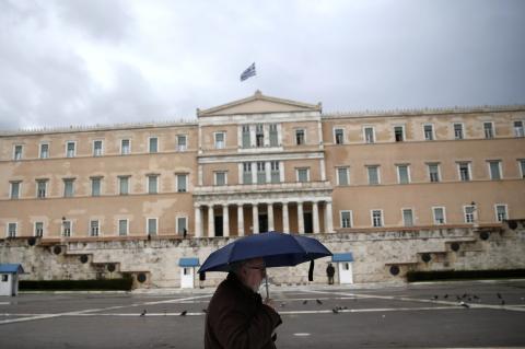 A man holding an umbrella makes his way in front of the Greek parliament during rainfall in Athens, January 29, 2015. PHOTO BY REUTERS/Alkis Konstantinidis
