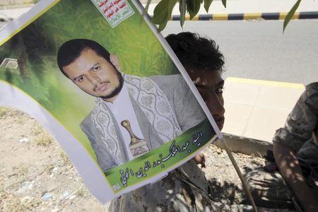 A youth dressed in military uniform holds up a poster of the Houthi movement's leader Abdel-Malek Badruddin al-Houthi as he and a friend sit under a tree after being stationed to provide security during celebrations marking the 25th anniversary of Yemen's unification, in Sanaa May 23, 2015. PHOTO BY REUTERS/Mohamed al-Sayaghi