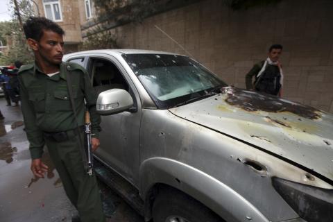 Policemen stand by a damaged car where a French man was assassinated, in Sanaa