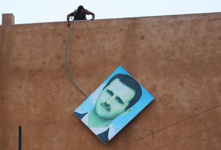 A member of al Qaeda's Nusra Front takes down a picture of Syria's President Bashar al-Assad in the northwestern city of Ariha, after a coalition of insurgent groups seized the area in Idlib province, May 29, 2015. PHOTO BY REUTERS/Ammar Abdullah