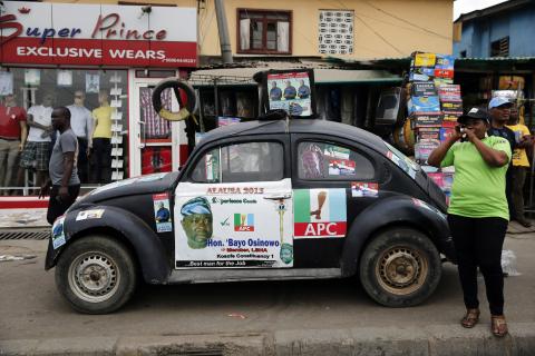 A woman talks on a mobile phone, near a car with election campaign posters for the All Progressives Congress (APC), parked in front of roadside stalls in the Oworonshoki district of Lagos, January 19, 2015. PHOTO BY REUTERS/Akintunde Akinleye
