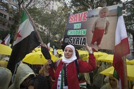 A protester stands in the rain near the United Nations Building and holds up a sign asking to save the children of Syria during the United Nations General Assembly in the Manhattan borough of New York, September 25, 2014. PHOTO BY REUTERS/Carlo Allegri
