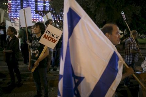 Left-wing protesters, one holding a placard bearing the logo of Peace Now, an Israeli NGO that tracks and opposes Jewish settlement in the occupied West Bank and East Jerusalem, take part in a rally in Tel Aviv, October 24, 2015. PHOTO BY REUTERS/Baz Ratner