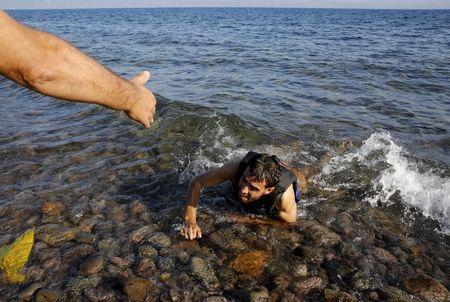 A local man helps a Syrian refugee who jumped off board from a dinghy as he swims exhausted at a beach on the Greek island of Lesbos, September 17, 2015. PHOTO BY REUTERS/Yannis Behrakis