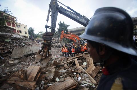 Rescue crew members watch as others use excavators to scour the debris for survivors at the site of a collapsed residential building in Mumbai